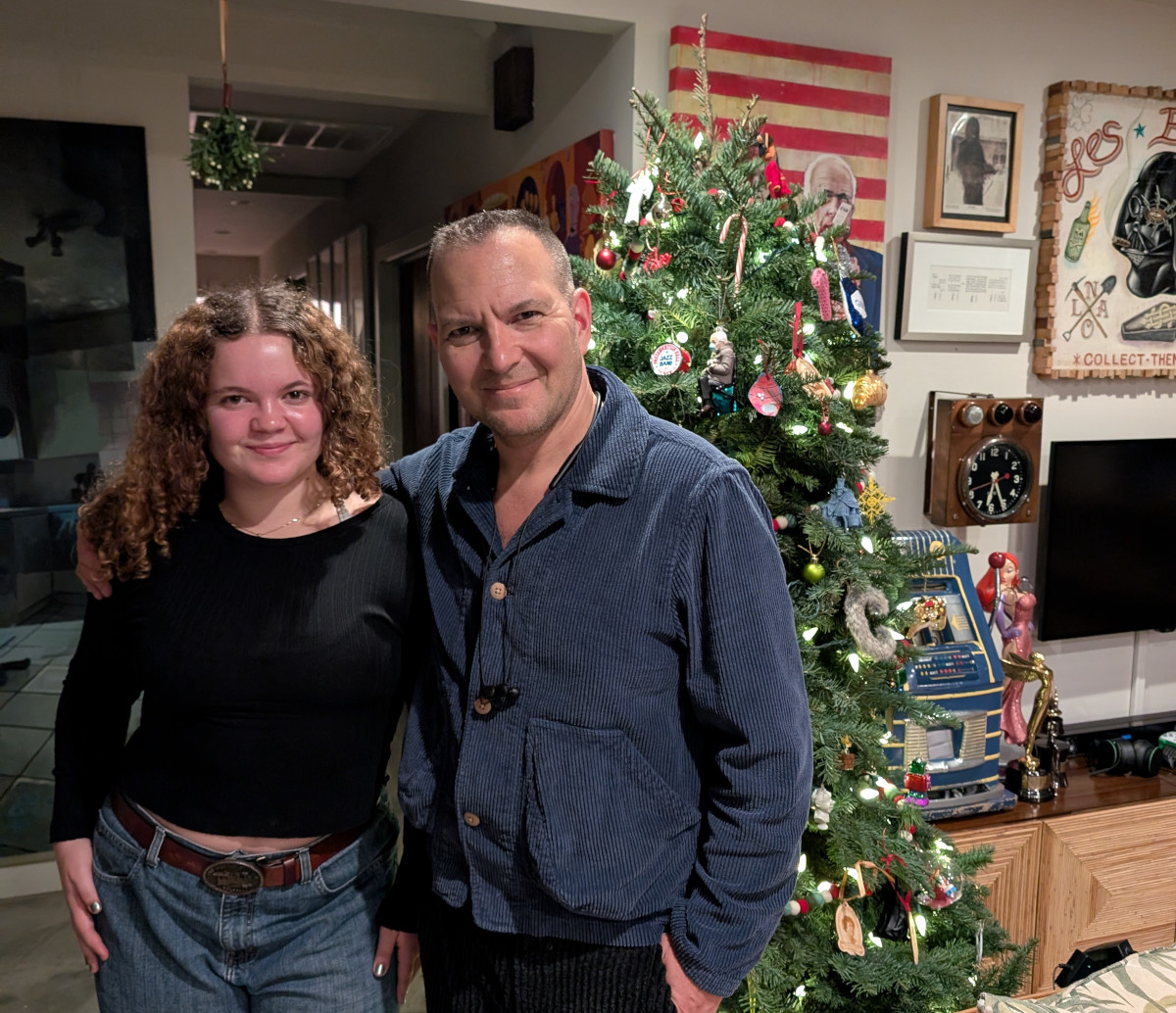My daughter Poesy and me standing in front of our Christmas tree at home. I have my arm around her shoulders.